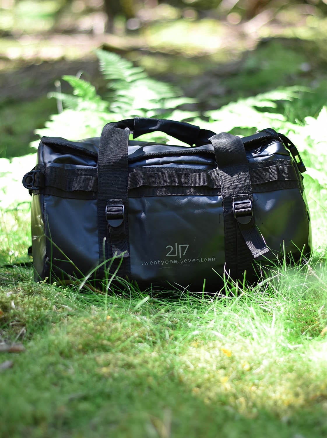 black tarpaulin duffle bag placed in green grass